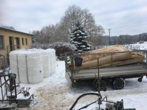 Reste der Alten Öltanks auf einem Anhänger. Daneben stehen die neuen, noch verpackten Tanks im Schnee.